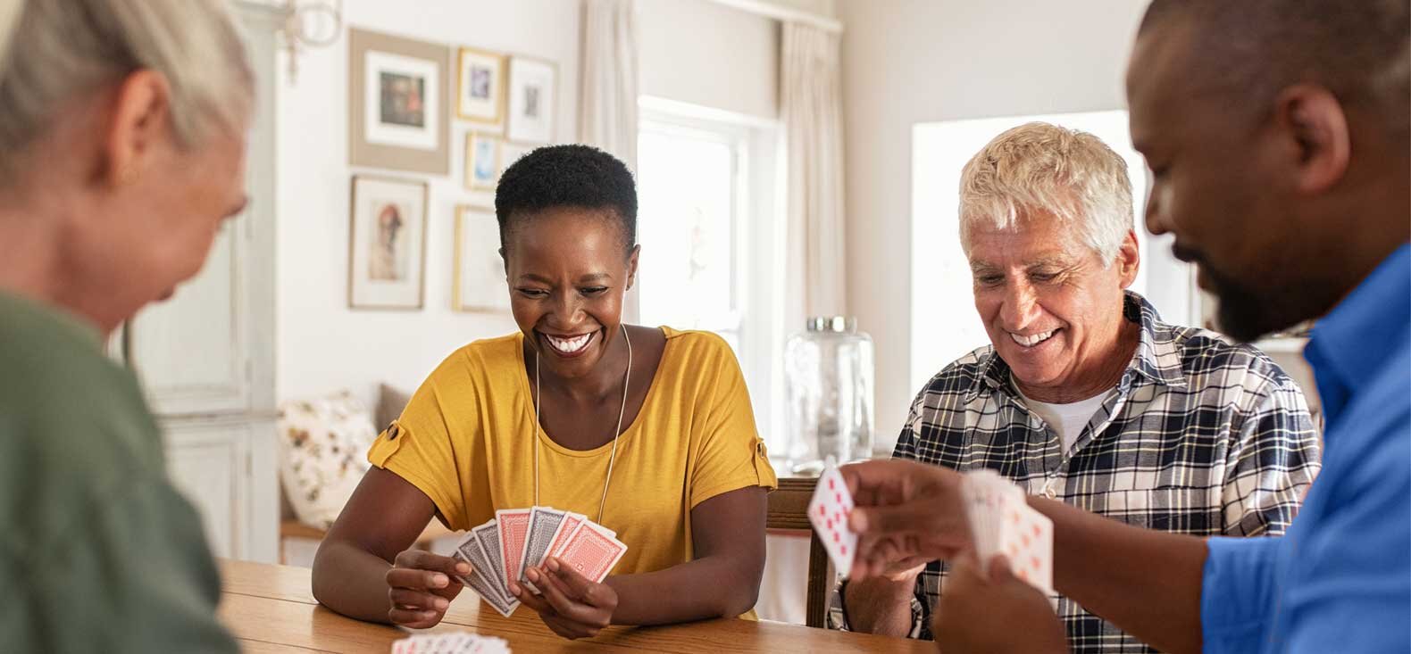 Four older adults socializing around table playing cards