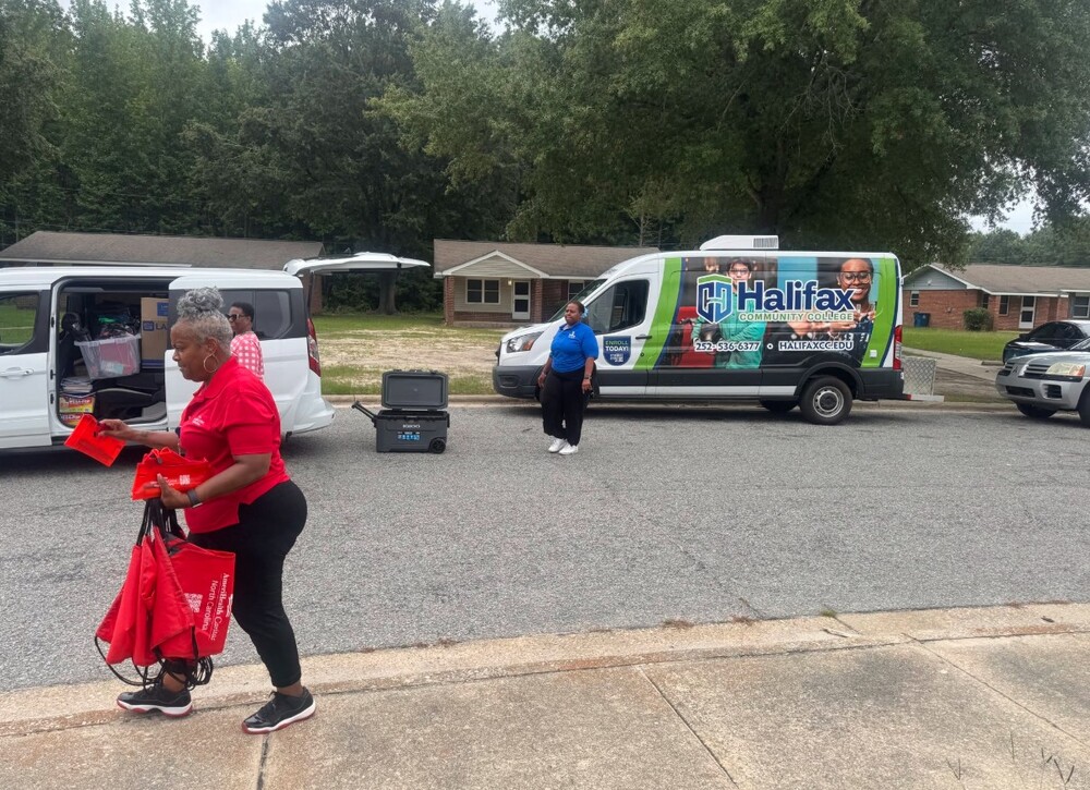 A woman walking away from two vans with school supplies in her hands.