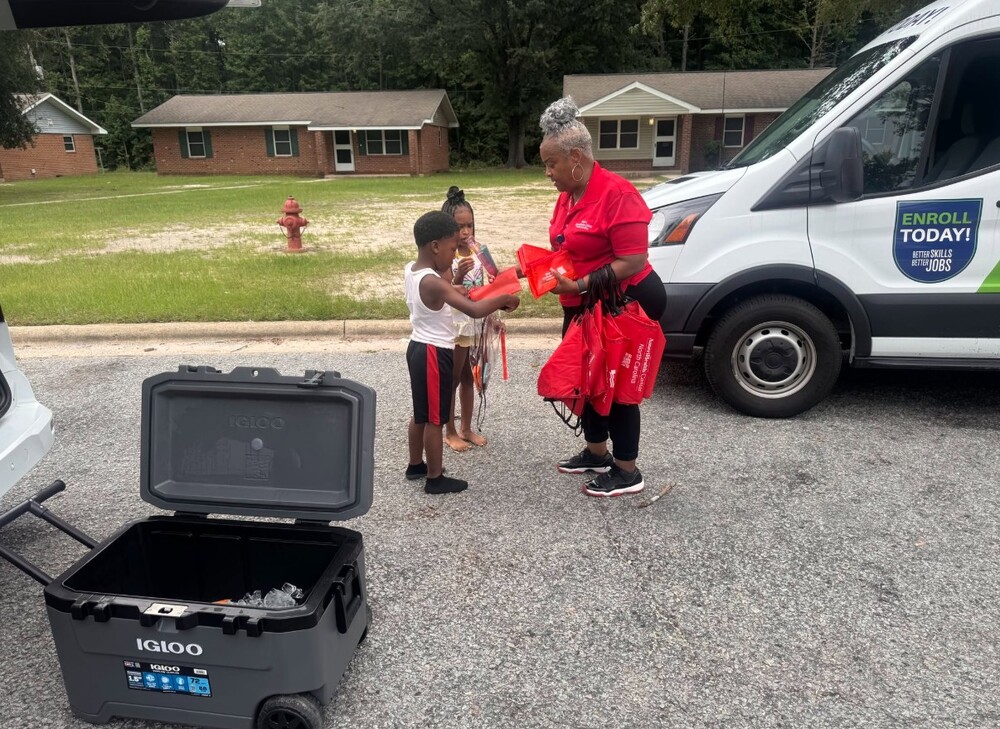 A woman handing school supplies to two young kids.