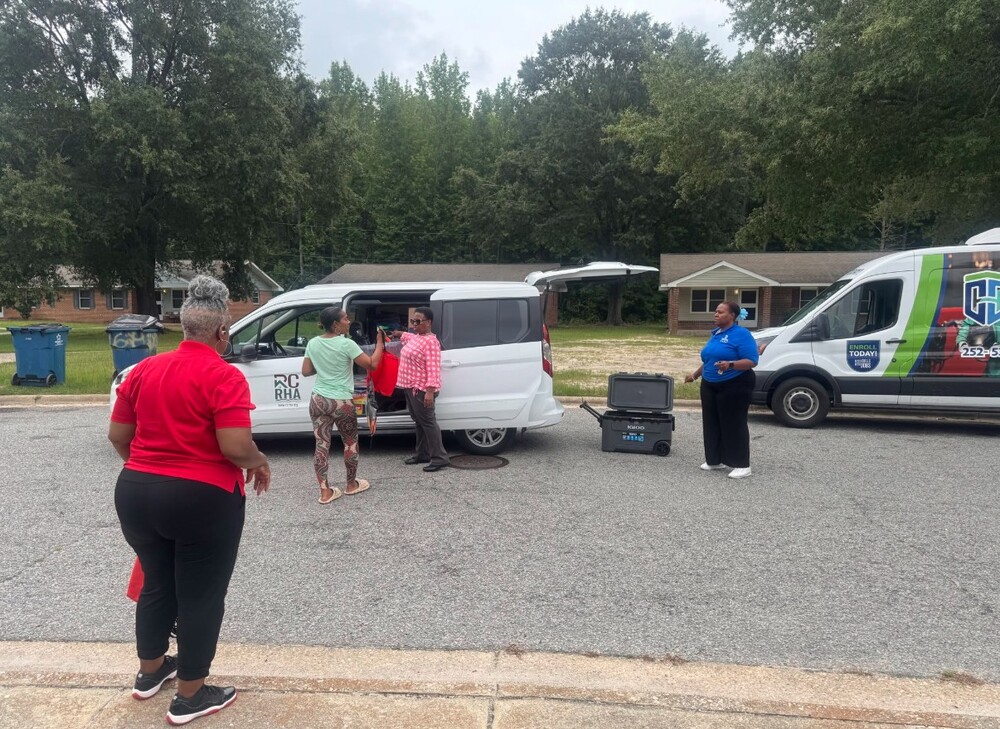 Four woman standing by vans getting school supplies out.