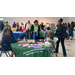 A group of people standing around visiting in a large room with tables.