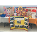 A table with assorted crafts and a cardboard sign with accreditation certificates.