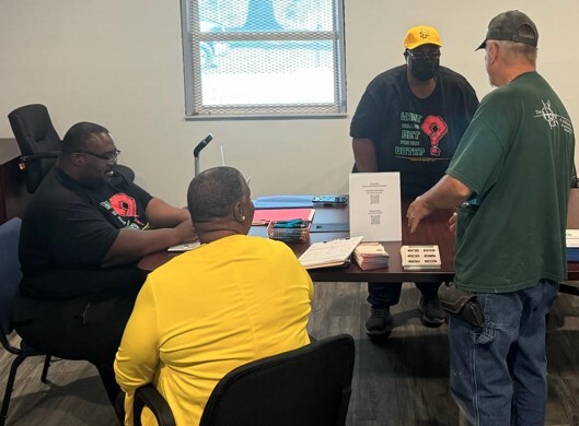 Agroupofmensittingaroundatable..jpg A group of men sitting around a table.