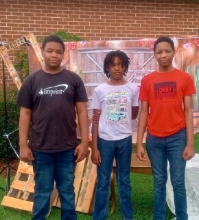 bootsontheground1.jpg Three boys standing and smiling for a photo.